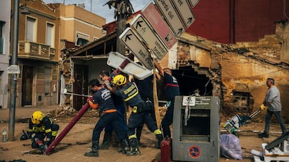 Varios bomberos sujetan un poste dañado por la dana.