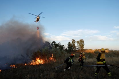 Agentes forestales se alejan tras una descarga de agua desde un helicóptero para sofocar un incendio en las afueras de Valmojado (Toledo), este jueves.