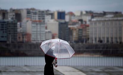 Una mujer camina este lunes por el paseo marítimo de A Coruña, cubierta con paraguas y mascarilla, en el comienzo de una semana inestable en lo meteorológico, con lluvias en la mayor parte del país.