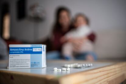 Una caja de amoxicilina en primer término, con una madre y su hija al fondo.