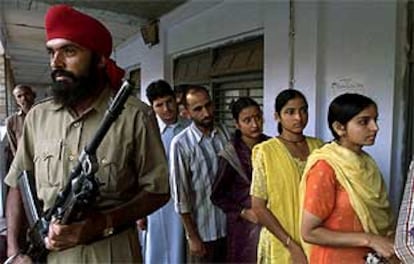 Un grupo de electores de Cachemira esperan para depositar su voto bajo la vigilancia de un soldado indio.