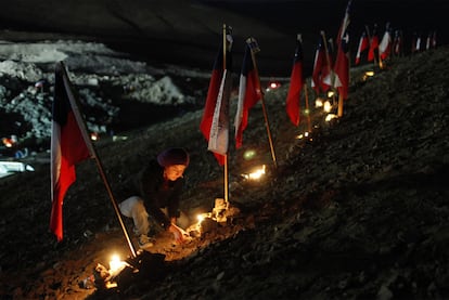 Una familiar de uno de los mineros encerrados enciende velas colocadas junto a banderas chilenas en el exterior de la mina.