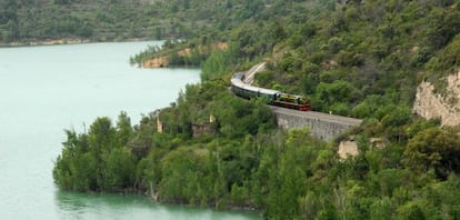 El tren atraviesa el pantano de Cellers, con apariencia de lago natural, en cuyo espejo de aguas tranquilas se reflejan los exuberantes bosques de ribera y las cumbres pirenaicas.