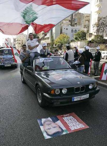 Un coche de seguidores del partido del ministro libanés de Industria, Pierre Gemayel, pasa por encima de un poster del presidente sirio Bashar al-Achad.