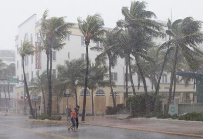 La gente camina por la calle mientras el viento y la lluvia empiezan a golpear ante la llegada del huracán a Miami.