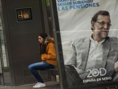 Una joven espera al autob&uacute;s en una marquesina con carteles electorales de Mariano Rajoy (azul) y Pedro S&aacute;nchez (rojo). 