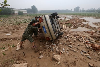 Varias personas empujan un coche que ha volcado durante una inundación en Xingtai, provincia de Hebei, China, el domingo 24 de julio. 
