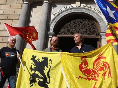 Desde la izquierda: cuatro personas sostienen bandera de Occitania, Flandes, Valonia y la estelada, ante el Palau de la Generalitat