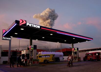 Una columna de humo y ceniza proveniente del volcán Mayon se eleva tras una gasolinera en Daraga en la provincia de Albay (Filipinas).