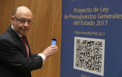 El ministro de Hacienda, Cristóbal Montoro, escanea con el móvl el código QR del proyecto de Ley de Presupuestos Generales del Estado (PGE) para 2017, poco antes de la rueda de prensa que ha ofrecido hoy en el Congreso para presentarlo.