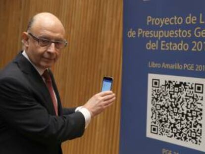 El ministro de Hacienda, Crist&oacute;bal Montoro, escanea con el m&oacute;vl el c&oacute;digo QR del proyecto de Ley de Presupuestos Generales del Estado (PGE) para 2017, poco antes de la rueda de prensa que ha ofrecido hoy en el Congreso para presentarlo. 