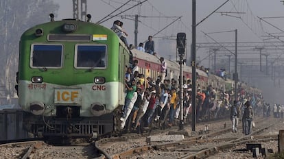 Varios pasajeros indios se sujetan a los vagones del tren durante su salida en una estación a las afueras de Nueva Delhi (India).