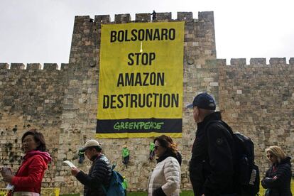 Un grupo de turistas pasa por delante de activistas de Greenpeace mientras cuelgan una pancarta con un mensaje dirigido a Jair Bolsonaro para reclamar el fin de la deforestación del Amazonas, en las murallas de la Ciudad Vieja de Jerusalén.