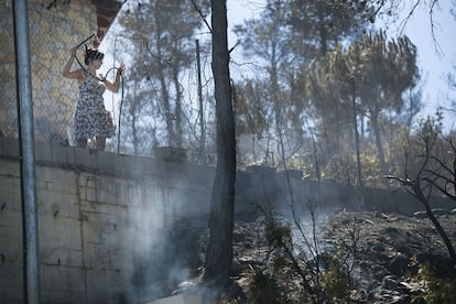 Una vecina enfría las partes aún calientes del incendio al lado de su casa con una manguera.