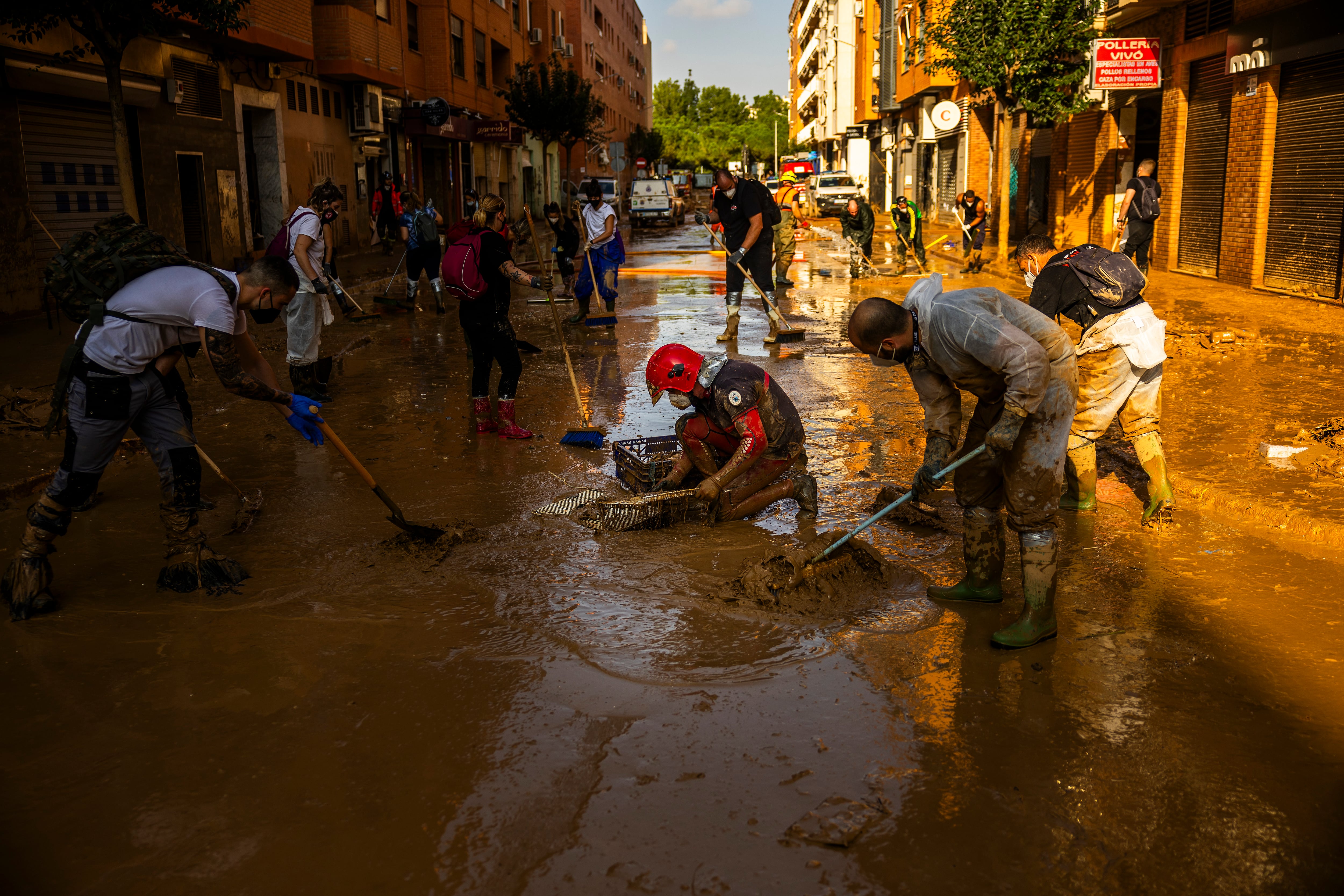 Un bombero y un grupo de voluntarios achican agua y barro en una alcantarilla en los alrededores de la avenida Blasco Ibáñez, en Catarroja. 