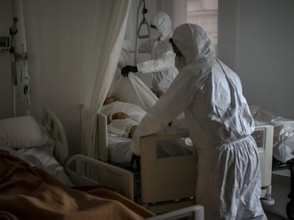 Trabajadores de una funeraria retiran el cuerpo de un anciano fallecido por coronavirus en un asilo mientras otro residente duerme al lado en su cama, en Barcelona.