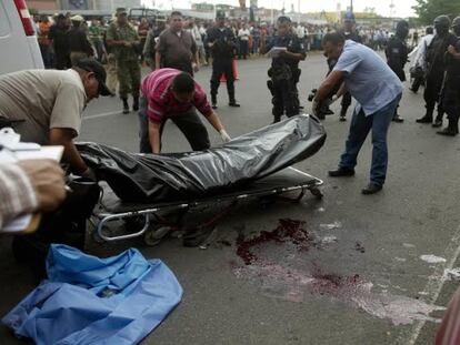 Forensics experts move the bodies of two police officers killed in Culiacán