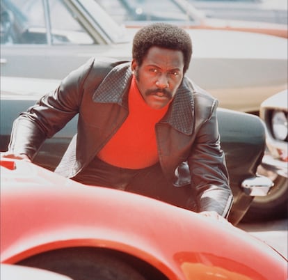 Richard Roundtree agachado detrás de un automóvil deportivo rojo en una escena de 'Shaft', 1971. La película blaxploitation, dirigida por Gordon Parks.