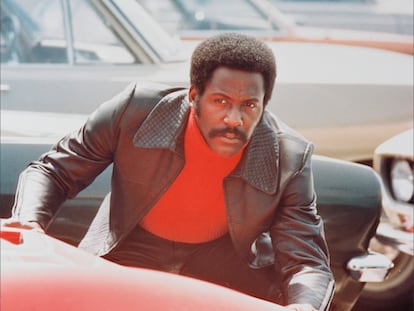 Richard Roundtree agachado detrás de un automóvil deportivo rojo en una escena de 'Shaft', 1971. La película blaxploitation, dirigida por Gordon Parks.