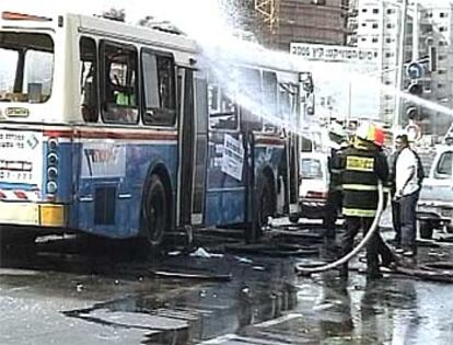 Los bomberos se afanan por apagar el fuego que consumía uno de los autobuses tras la explosión.