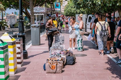 Un vendedor ambulante en una calle con muchos turistas vende bolsos falsificados en Marbella.