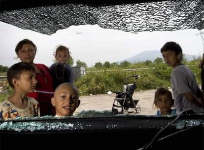 Unos niños miran por la ventanilla rota de un coche en el campamento gitano de Casoria (Nápoles).