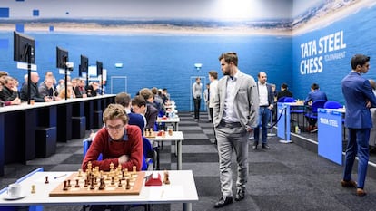 Magnus Carlsen pasea por la sala de juego en Wijk aan Zee durante su partida de este lunes; en primer plano, el español David Antón, participante en el Torneo B