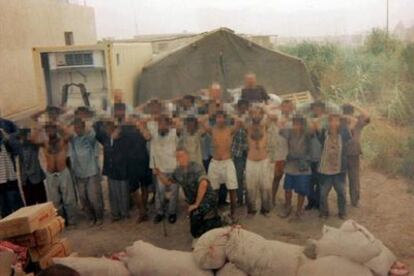 Dos soldados posan en esta fotografía con el grupo de iraquiés detenidos por robar leche en polvo. De hecho, los sacos del delito aparecen en primer término. Las Convenciones de Ginebra sobre el derecho de los prisioneros de guerra prohíben expresamente tomar imágenes de los prisioneros a modo de <i>souvenir.</i>