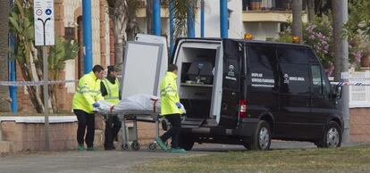 Operarios de los servicios fúnebres acompañados de un guardia civil trasladan el cadáver de la mujer asesinada en Rincón de la Victoria.
