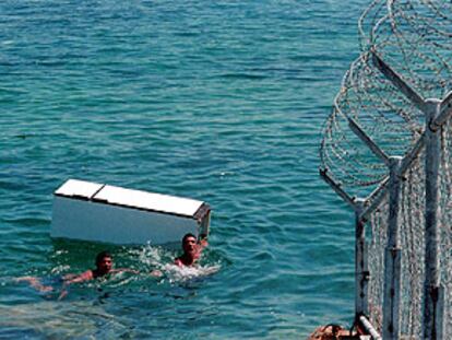 Dos marroquíes pasan un frigorífico a nado al otro lado de la frontera de Tarajasl, en Ceuta.