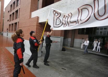 Varios agentes de la Ertzaintza retiran un cartel a favor de Bildu de un colegio electoral en San Sebastián.