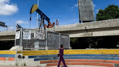 Mulher caminha diante de uma bomba de extração de petróleo na Universidade de Caracas