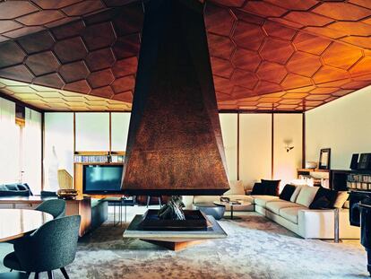 La chimenea de cobre martilleado a mano preside el salón de la casa, dividido en cuatro espacios y cubierto por un techo de madera de nogal con forma de panel de abeja.|