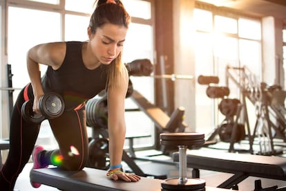 <strong>Extensión o patada de tríceps.</strong>  </br>"Se inicia de pie. Adelantamos una pierna y la dejamos semiflexionada. Inclinamos el torso hacia delante. En esa posición, levantamos y bajamos la mancuerna, tirando del codo hacia detrás. El ejercicio puede realizarse también apoyando la rodilla y brazo contraria sobre un banco, como en la imagen. El ritmo de movimiento debe ser lento". </br> <strong>Extensión vertical sobre la cabeza.</strong> </br>"De nuevo, arrancamos de pie y con una pierna adelantada y semiflexionada. Agarramos la mancuerna con ambas manos, la posamos en la base del cráneo con los codos pegados a la cabeza. De esa postura, la elevamos hacia el cielo extendiendo los codos". Para evitar que la espalda se arquee, es imprescindible activar los abdominales.