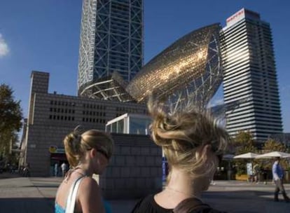 Las escamas de bronce del <i>Peix d'Or,</i> escultura de Frank Gehry de 1992, brillan al sol en el puerto Olímpico de Barcelona, con las torres del edificio del hotel Arts y la torre Mapfre al fondo<b>.</b>