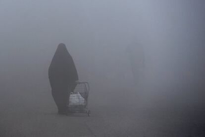 Una mujer camina con un carrito de compra en medio de la densa niebla en la ciudad santa de Nayaf (Irak).