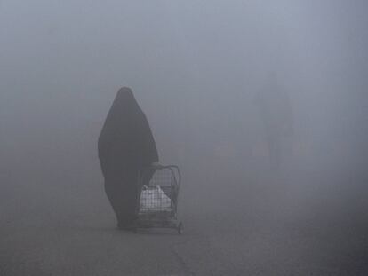 Una mujer camina con un carrito de compra en medio de la densa niebla en la ciudad santa de Nayaf (Irak).