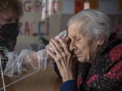 Una anciana saluda a su hija a través de una pantalla de plástico en una residencia italiana.