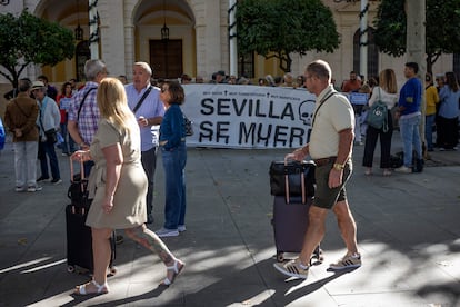 Dos turistas pasan delante de la protesta de colectivos vecinales contra el aumento de los pisos turísticos en Sevilla.