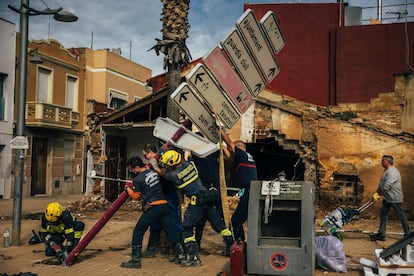 Varios bomberos sujetan un poste dañado por la dana, mientras cortan el pie para poder retirarlo, este martes en Alfafar.