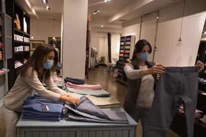 La propietaria (izquierda) y una clienta, ambas con mascarilla, miran ropa de hombre en Lester, una tienda de moda de Madrid que ha reabierto este lunes.