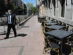 Un hombre con mascarilla pasa junto a una terraza cerrada de un bar en Madrid.