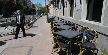 Un hombre con mascarilla pasa junto a una terraza cerrada de un bar en Madrid.