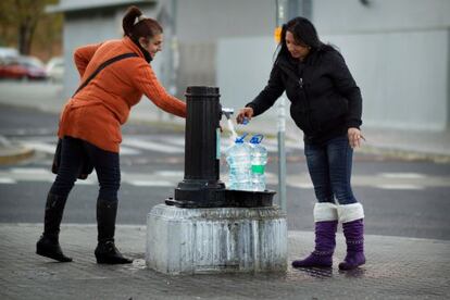 Dos vecinas de la corrala sevillana La utop&iacute;a, que no tiene suministro, cogen agua en una fuente de la ciudad.