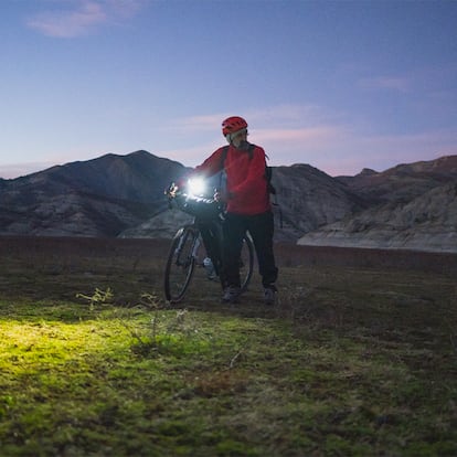Un hombre con su bici en medio de la montaña anocheciendo.