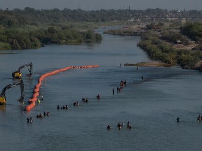 A caravan wades past a string of buoys, being constructed to deter migrants crossing through the Rio Grande, as they look for an opening in the concertina wire to enter into Eagle Pass, Texas, on July 27, 2023