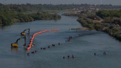 Una caravana de migrantes pasa junto a una serie de boyas que se colocan en el río Bravo