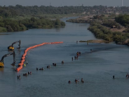 Una caravana de migrantes pasa junto a una serie de boyas que se colocan en el río Bravo.
