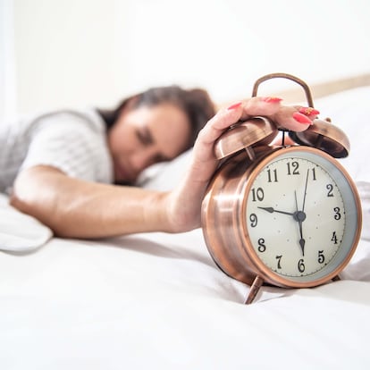 A loud alarm clock woke a young woman, she turns it off and continues to sleep.