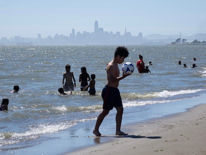 A young man plays with a soccer ball while bathers cool off in Alameda, California (USA), on June 5, 2024. 